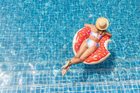 Téléchargez les photos : Beautiful young woman with inflatable donut ring relaxing in swimming pool. Summer vacation. Top view with copy space - en image libre de droit