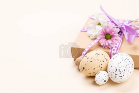 Foto de Gift box, Easter eggs and flowers on a beige background with space for your greetings - Imagen libre de derechos