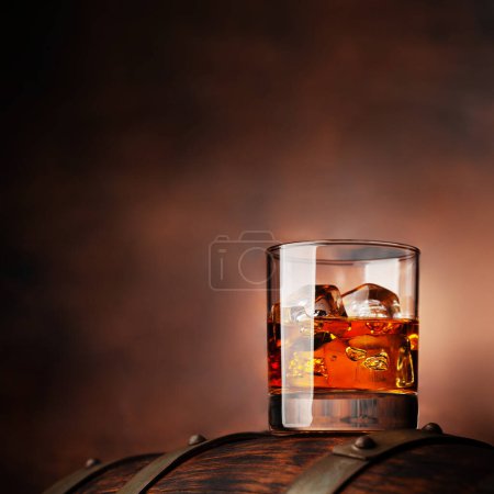 Photo for Glass of whiskey with ice cubes on the old barrel. With copy space on wooden background - Royalty Free Image