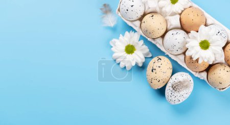 Foto de Huevos de Pascua empaquetan y flores sobre un fondo azul con espacio para sus saludos. Puesta plana - Imagen libre de derechos