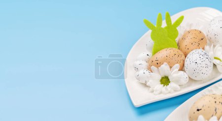 Foto de Huevos de Pascua y flores en plato sobre fondo azul con espacio para copiar - Imagen libre de derechos