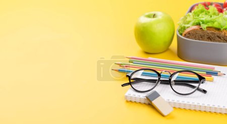 Foto de Material escolar, papelería y lonchera sobre fondo amarillo. Educación y nutrición. Con espacio en blanco para su texto - Imagen libre de derechos