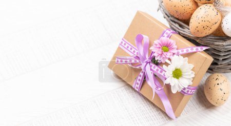 Foto de Caja de regalo con flores y canasta de huevos de Pascua sobre fondo de madera con espacio para tus saludos - Imagen libre de derechos