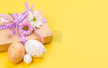 Foto de Caja de regalo, huevos de Pascua y flores sobre fondo amarillo con espacio para tus saludos - Imagen libre de derechos