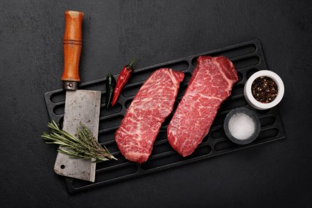 Foto de Prime marbled beef steaks and spices. Raw striploin steak. Flat lay - Imagen libre de derechos