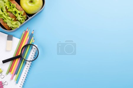 Foto de Material escolar, papelería y lonchera sobre fondo azul. Educación y nutrición. Piso con espacio en blanco - Imagen libre de derechos