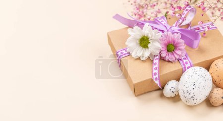 Foto de Caja de regalo, huevos de Pascua y flores sobre fondo beige con espacio para tus saludos - Imagen libre de derechos