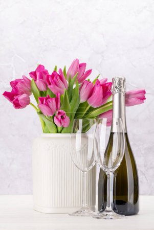 Foto de Ramo de flores de tulipán rosa fresco y champán. En mesa de madera blanca con espacio para copiar - Imagen libre de derechos