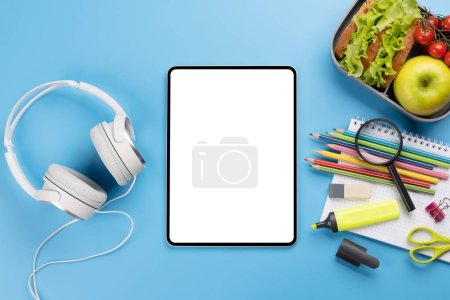Photo for Tablet with blank screen, school supplies, stationery, and lunch box on blue background. Education and nutrition. Flat lay with blank space for your text or app - Royalty Free Image