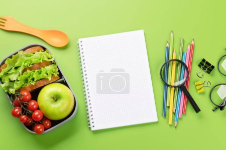 Foto de Material escolar, papelería y lonchera sobre fondo verde. Educación y nutrición. Piso con espacio en blanco - Imagen libre de derechos