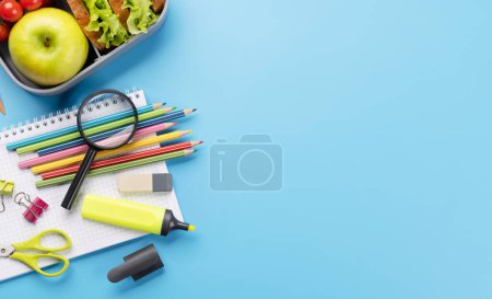 Téléchargez les photos : Fournitures scolaires, papeterie et boîte à lunch sur fond bleu. Éducation et nutrition. Pose plate avec espace vide - en image libre de droit