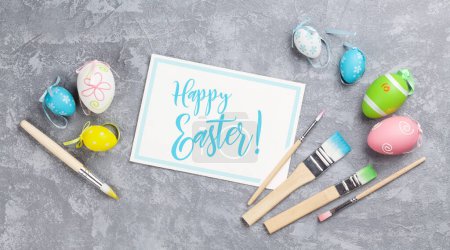 Foto de Huevos coloridos de Pascua, tarjeta de felicitación y cepillos en la mesa de piedra. Vista superior - Imagen libre de derechos