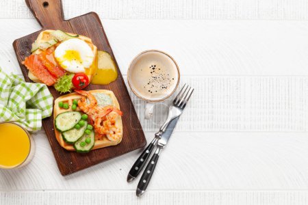 Foto de Desayuno gofres con huevos fritos, salmón, tocino, pepino y gambas. Vista superior plano con café, zumo de naranja y espacio de copia - Imagen libre de derechos