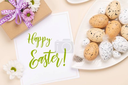 Téléchargez les photos : Oeufs de Pâques, fleurs et coffret cadeau sur fond beige. Pose plate avec carte de vœux de Pâques - en image libre de droit