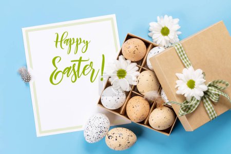 Foto de Huevos de Pascua paquete y flores sobre un fondo azul con tarjeta de felicitación de Pascua. Puesta plana - Imagen libre de derechos