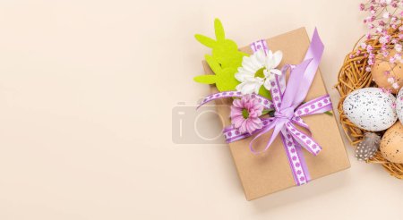 Foto de Caja de regalo, huevos de Pascua y flores sobre fondo beige con espacio para tus saludos. Puesta plana - Imagen libre de derechos
