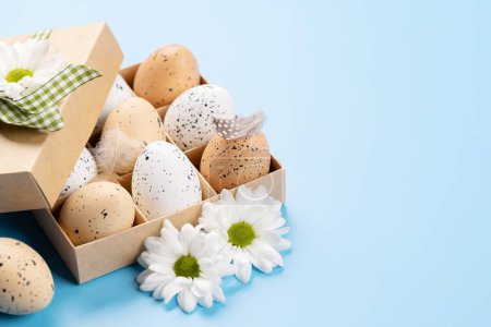 Téléchargez les photos : Coffret cadeau, oeufs de Pâques et fleurs sur fond bleu avec espace pour vos salutations - en image libre de droit