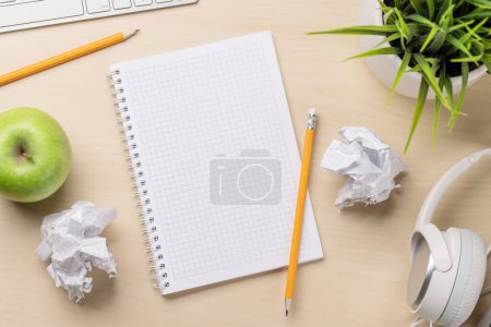 Photo for Top view of blank notepad, keyboard, headphones, apple and crumpled papers on desk, depicting unsuccessful attempts at writing - Royalty Free Image