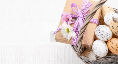 Téléchargez les photos : Gift box with flowers and Easter eggs basket on a wooden background with space for your greetings - en image libre de droit