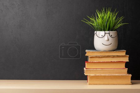 Téléchargez les photos : Empilement de vieux livres et de plantes en pot sur la table devant le mur de tableau. Avec de l'espace pour votre texte. Concept d'apprentissage et de travail - en image libre de droit