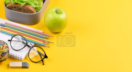 Téléchargez les photos : Fournitures scolaires, papeterie et boîte à lunch sur fond jaune. Éducation et nutrition. Avec espace vide pour votre texte - en image libre de droit