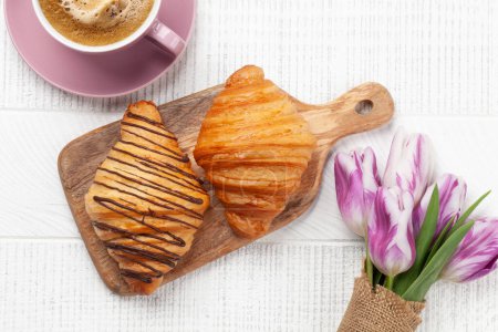 Foto de Varios croissants y café sobre tabla de madera y ramo de tulipanes. Desayuno francés. Vista superior plano laico - Imagen libre de derechos