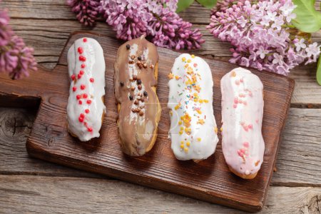 Photo for Various eclair dessert. On wooden table with lilac flowers - Royalty Free Image