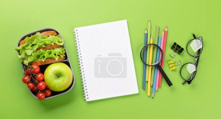 Foto de School supplies, stationery, and lunch box on green background. Education and nutrition. Flat lay with blank space - Imagen libre de derechos