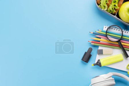 Foto de School supplies, stationery, and lunch box on blue background. Education and nutrition. Flat lay with blank space - Imagen libre de derechos