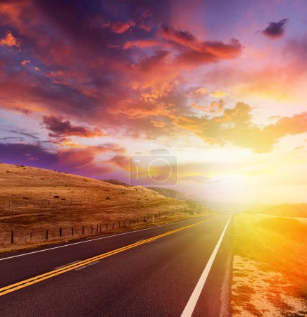 Téléchargez les photos : Route asphaltée vide dans un paysage rural au coucher du soleil avec un ciel spectaculaire - en image libre de droit