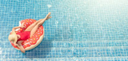 Téléchargez les photos : Belle jeune femme avec anneau de beignet gonflable relaxant dans la piscine. Vacances d'été - en image libre de droit