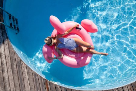 Téléchargez les photos : Femme relaxante sur anneau gonflable rose flamant rose. Vacances ensoleillées avec piscine. Pose plate - en image libre de droit