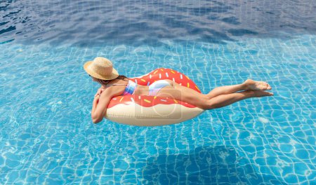 Foto de Hermosa mujer joven con anillo de rosquilla inflable relajándose en la piscina. Vacaciones de verano - Imagen libre de derechos