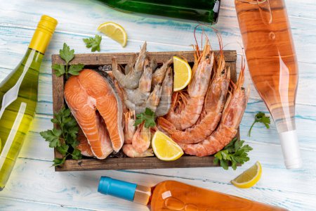 Téléchargez les photos : Une vue de dessus des fruits de mer frais tels que les crevettes, le homard et les steaks de truite, accompagnés de vin blanc et rose - en image libre de droit
