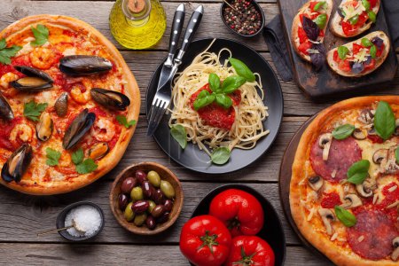 Foto de Cocina italiana. Pastas, pizza, aceitunas y tostadas antipasto. Colocación plana sobre mesa de madera - Imagen libre de derechos