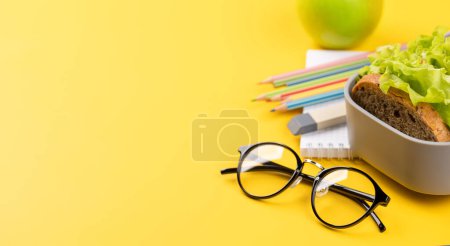 Téléchargez les photos : School supplies, stationery, and lunch box on yellow background. Education and nutrition. With blank space for your text - en image libre de droit