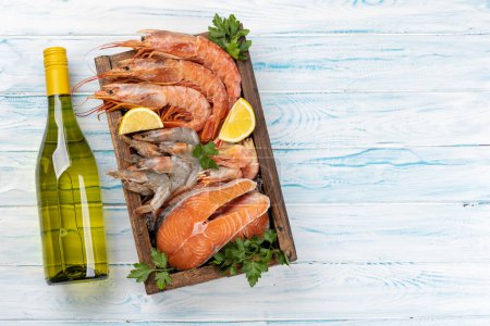 Téléchargez les photos : Une vue sur les fruits de mer frais tels que les crevettes, le homard et les steaks de truite, accompagnés de vin blanc. Pose plate avec espace de copie - en image libre de droit