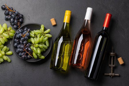 Photo for A top view of a wine bottles, grapes, corkscrew, and wine corks on a table. Flat lay - Royalty Free Image