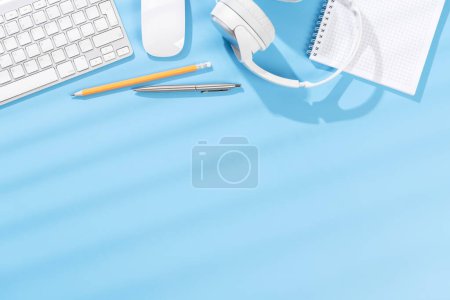 Foto de Escritorio de oficina de vista superior con teclado, suministros de oficina y auriculares. Espacio de trabajo plano con luz soleada y espacio de copia - Imagen libre de derechos
