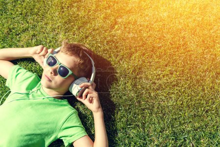 Téléchargez les photos : Un garçon se relaxant sur l'herbe, écoutant de la musique avec des écouteurs - en image libre de droit