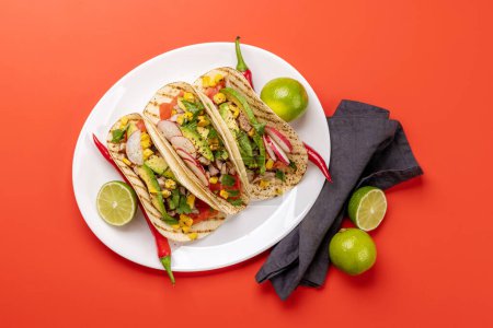 Mexican food featuring tacos with meat and grilled vegetables. Flat lay over red