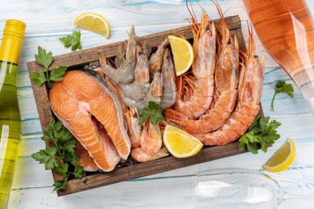 Téléchargez les photos : Une vue de dessus des fruits de mer frais tels que les crevettes, le homard et les steaks de truite, accompagnés de vin blanc et rose - en image libre de droit