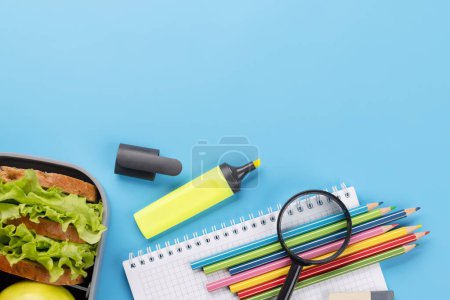 Foto de School supplies, stationery, and lunch box on blue background. Education and nutrition. Flat lay with blank space - Imagen libre de derechos