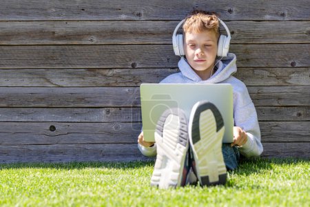 Foto de Un niño usando un portátil y auriculares al aire libre. Concepto de educación o entretenimiento - Imagen libre de derechos