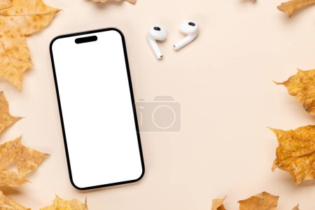 Téléchargez les photos : Smartphone avec écran blanc sur une table entourée de feuilles de nature d'automne, maquette design parfaite avec espace de copie - en image libre de droit