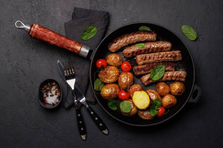 Téléchargez les photos : Délicieuses saucisses grillées et pommes de terre dans une poêle à frire pétillante. Pose plate - en image libre de droit