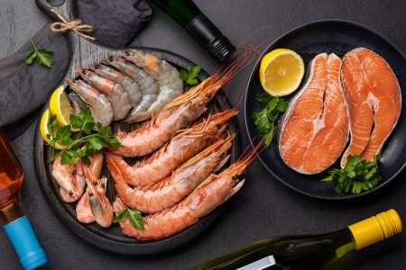Photo for A top view of fresh seafood such as shrimp, langoustines, and trout steaks, accompanied by white and rose wine. Flat lay - Royalty Free Image