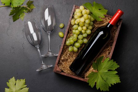 Foto de Botella de vino tinto y uvas frescas, presentadas en una caja de madera rústica. Puesta plana - Imagen libre de derechos