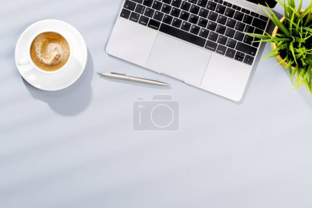 Foto de Escritorio de oficina de vista superior con computadora portátil, suministros de oficina y café. Espacio de trabajo plano con luz soleada y espacio de copia - Imagen libre de derechos
