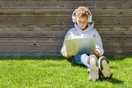 Foto de Un niño usando un portátil y auriculares al aire libre. Concepto de educación o entretenimiento - Imagen libre de derechos